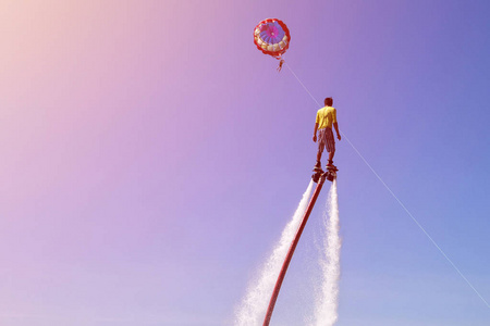 人骑在海滩上的 flyboard 与蓝天和降落伞的背景