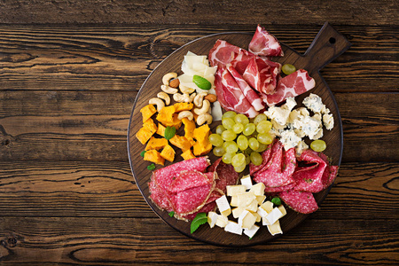 反胃餐饮盘与培根牛肉干，香肠，蓝色奶酪和葡萄在木制背景。 顶部视图