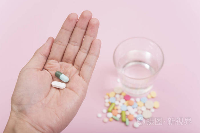 粉红色背景的手捧药和水杯