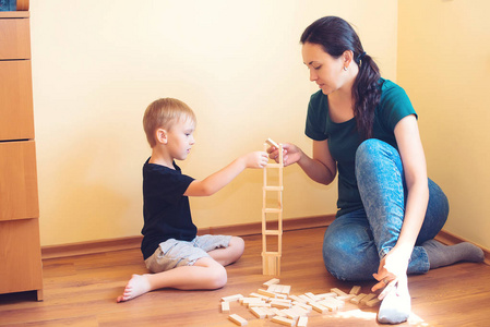 年轻的母亲和她的儿子在室内玩木块。 幸福的家庭花时间在家里。