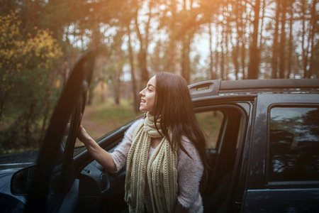 在汽车背景的长发黑发。女模特穿着毛衣和围巾。秋天的概念。秋天森林旅途由汽车