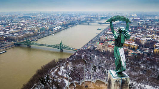 布达佩斯, 匈牙利空中全景的白雪皑皑的布达佩斯与自由女神像, 自由桥和多瑙河的背景从盖勒特山在一个多云的冬日里采取