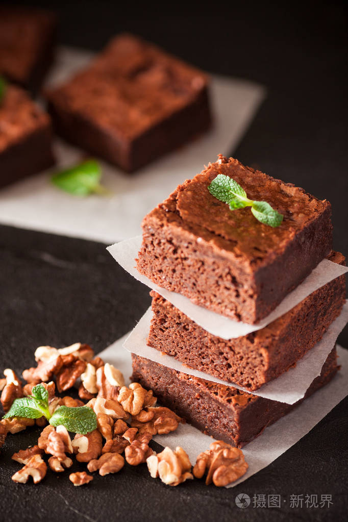 巧克力布朗尼方形块在白色的盘子与核桃装饰与薄荷叶和可可黑色背景