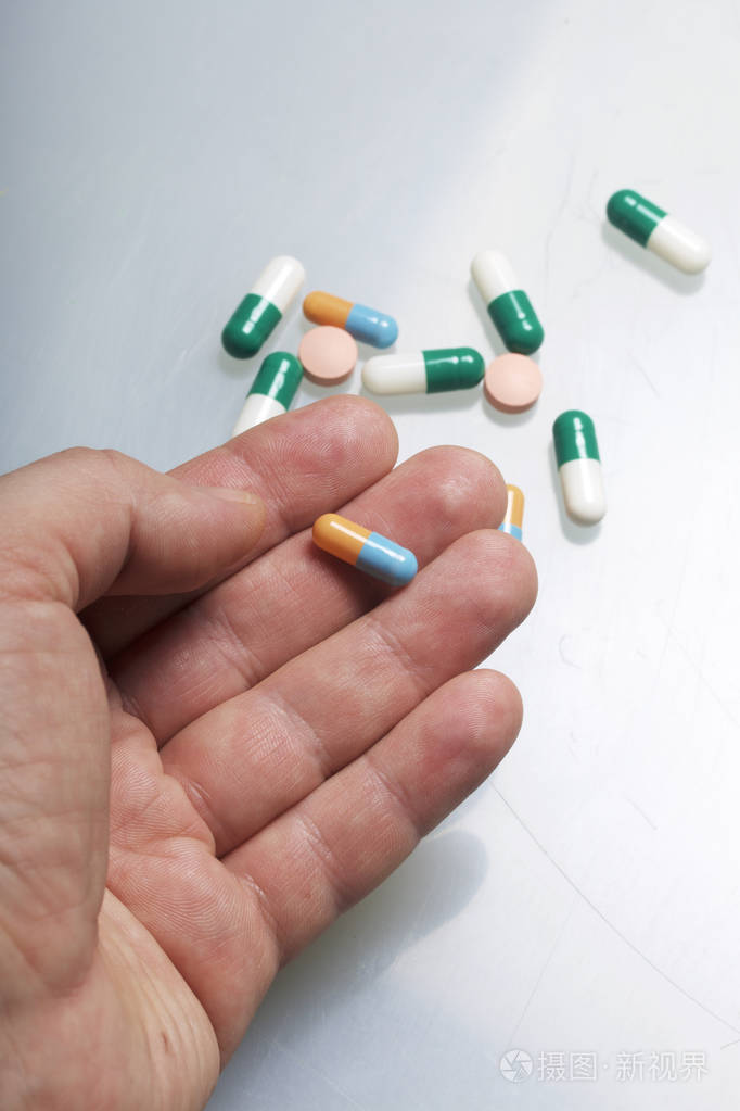 一个男人手里拿着一颗药丸桌子旁边是散落的多色药片