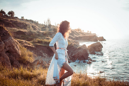 年轻女子穿着漂亮的白色连衣裙在早晨的海滩上散步。 适合女性在日出期间玩得很开心。