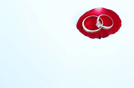 在白色背景下，在红色玫瑰花瓣上用复制空间关闭婚戒。
