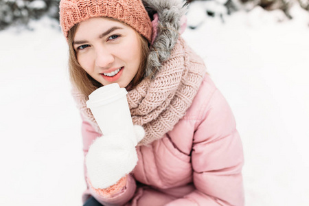一个美丽的年轻女孩的肖像在白色针织手套, 户外, 拿着一个热饮料的纸杯, 明亮的冬日. 女人微笑着, 是幸福的, 关闭, 在第一
