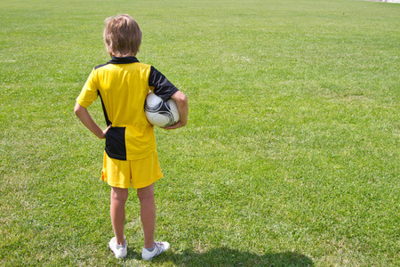 快乐的十几岁男孩手里拿着一个足球在体育场的背景下。 培训