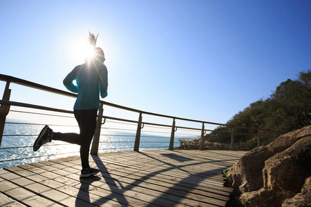 运动的女跑步者日出时在海滨木板路上跑步