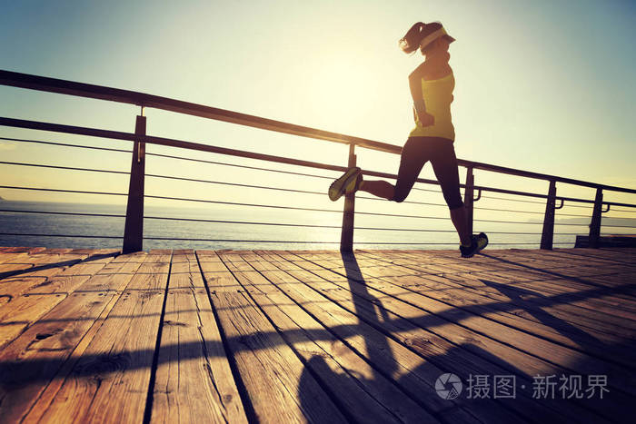 运动健身女跑步者日出时在海滨木板路上跑步
