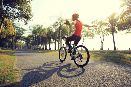 骑自行车的妇女骑自行车，张开双臂在热带公园里