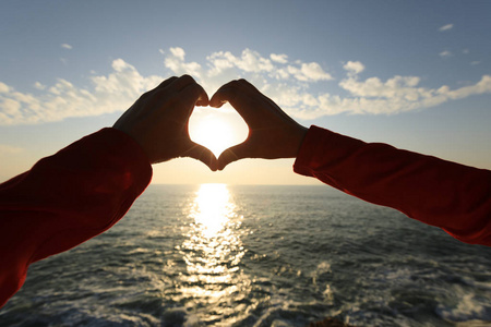统治者在人类双手人类的双手在日出的天空上制造心形图案照片