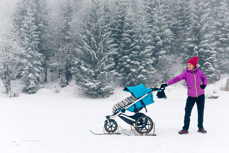 母亲与婴儿推车在冬天森林里享受母性