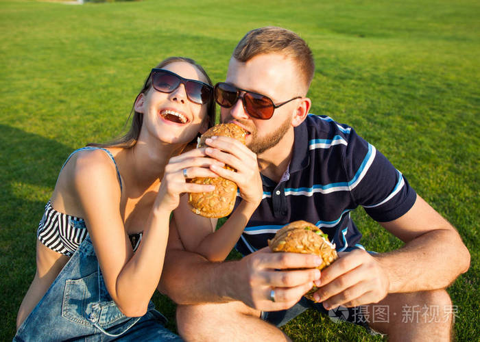 情侣坐在草地上的公园和吃 sandw