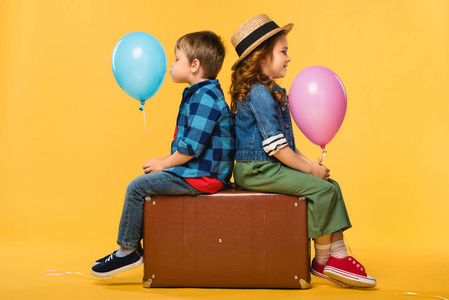儿童侧视，气球坐在皮手提箱上，孤立在黄色上