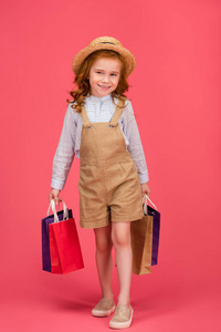 微笑的孩子穿着休闲服装，购物袋被隔离在粉红色