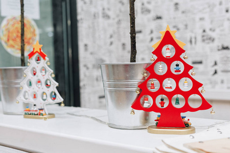 两棵红色和白色的装饰圣诞树站在金属背旁边的架子上，上面有小树，背景是像报纸一样的壁纸。