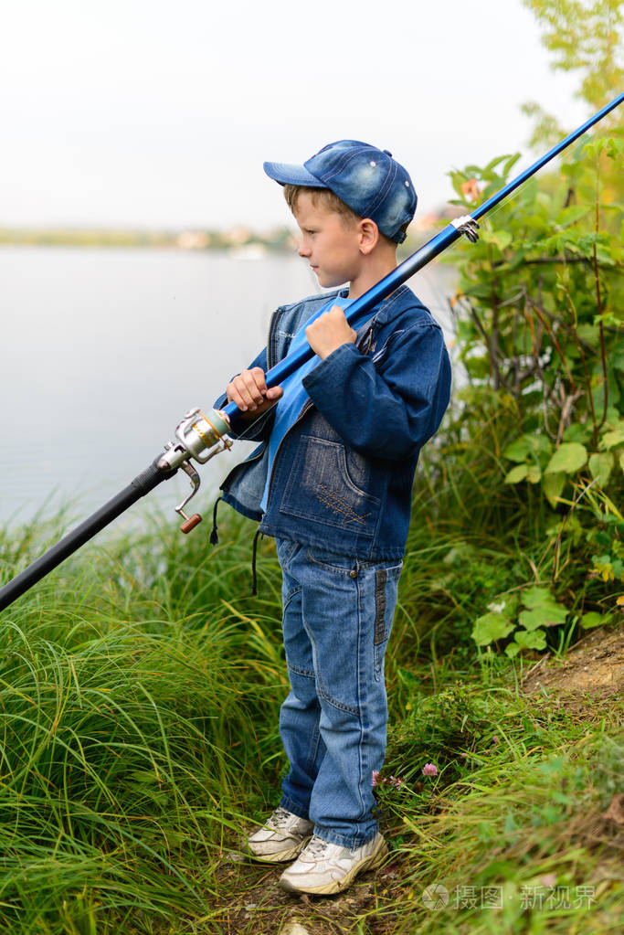 河岸边的渔夫男孩手里拿着钓竿