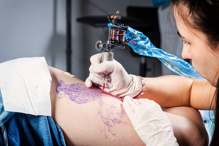 由专业艺术家制作的纹身师正在一个创意设计工作室里用机器纹身身体的女人