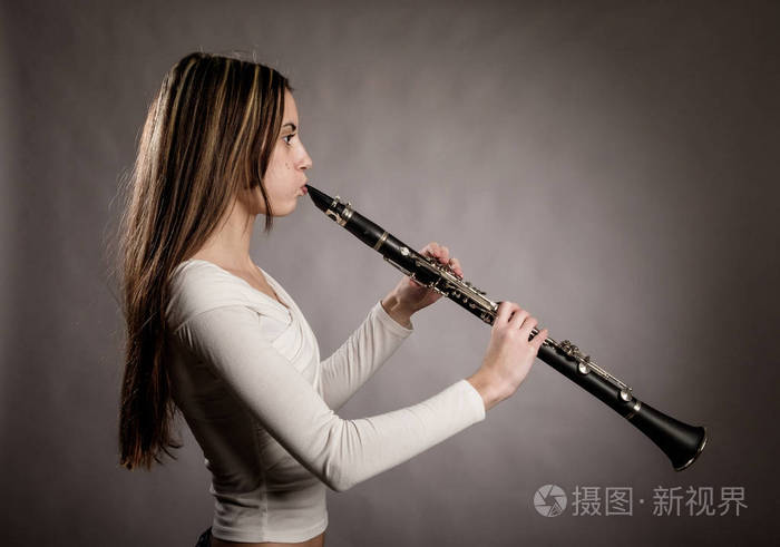在灰色背景下演奏单簧管的年轻女子