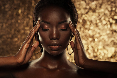 时尚工作室肖像一个非凡美丽的非洲裔美国人的模型与闭合的眼睛在金黄背景