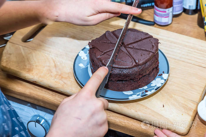 特写十几岁的男孩手切割板上的巧克力蛋糕在木板上用刀