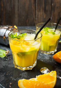 冷酒精夏天柑橘鸡尾酒与橙色和薄荷在玻璃和在黑暗的石头背景。鸡尾酒制作棒工具, 摇酒器, 薄荷叶