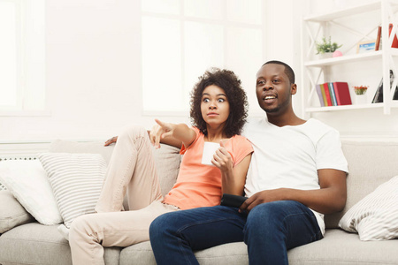 惊讶的非洲裔美国年轻夫妇在家看电视
