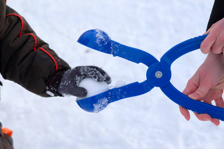 妈妈用塑料夹子雪球为孩子雕刻雪球。 手拿雪球