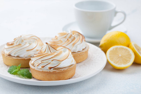 柠檬 tartlets 与蛋白酥饼在老式的白色盘子和杯茶在石桌上。淡蓝色背景下的美味佳肴