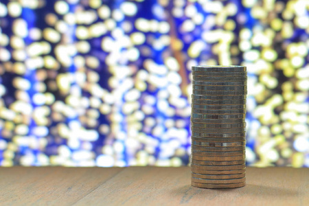 单柱硬币堆叠在木桌上，黄色的焦点灯在蓝色的夜晚背景。 有关商业储蓄及金钱的概念