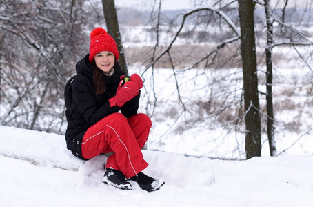 一个穿着鲜艳冬装的年轻女孩，在白雪皑皑的冬日风景中再次享受一杯茶