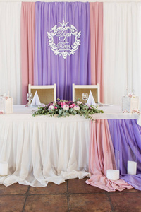 在餐厅提供婚宴餐桌，装饰白色粉红色和紫色材料，白色和粉红色的花朵和绿色植物。 新婚夫妇
