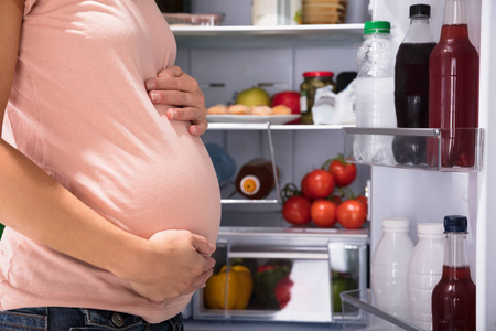 接近孕妇站在冰箱旁充满健康食物