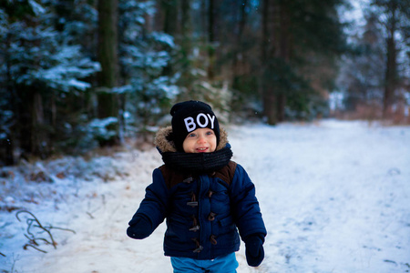 一个两岁的小男孩穿着蓝色夹克在冬天的森林里散步。