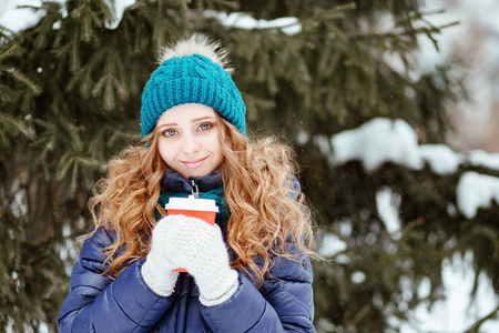 冬天在公园或树林里散步。 那个年轻漂亮的女孩，穿着温暖的帽子和一件羽绒垫外套的蓝色眼睛的金发女孩，用雪花手套抓住了一只手。 有降
