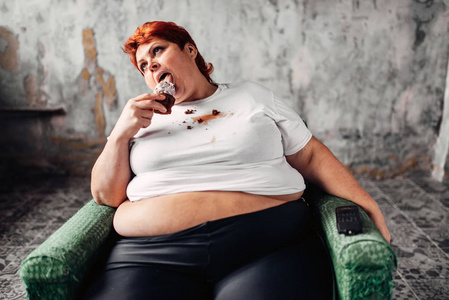 超重妇女坐在扶手椅上吃甜蛋糕,懒惰,肥胖和不健康的食物饮食观念照片