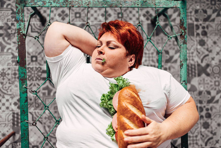 胖女人在床上吃三明治，不健康的生活方式和肥胖的概念