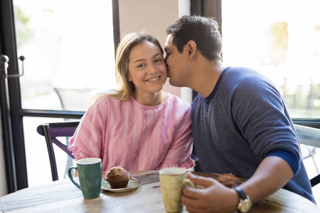 一幅可爱的年轻女人的肖像，她和男朋友在餐馆吃早餐，并在脸颊上亲吻
