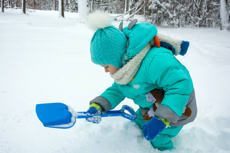 一个孩子在冬天的公园里玩耍, 用铲子铲雪