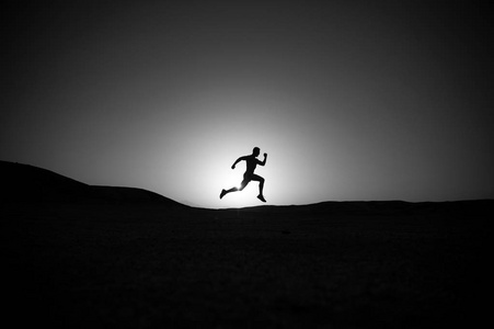 夕阳下奔跑的人的剪影,炽热的天空背景,在山区运动和娱乐的未来,成功