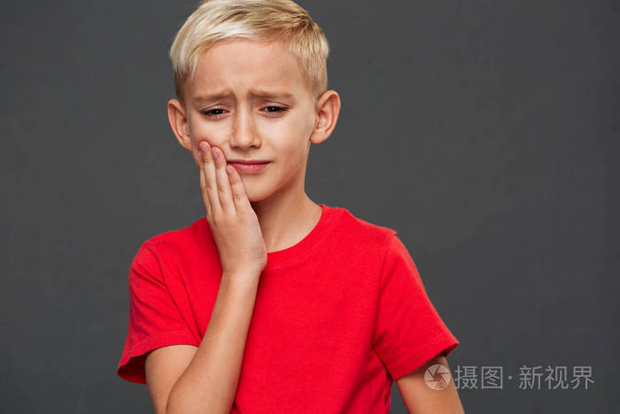 悲伤的小男孩的形象牙痛站在灰色的背景上孤立往旁边看