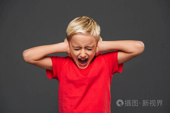 尖叫的小男孩孩子站在灰色背景上用手遮住耳朵