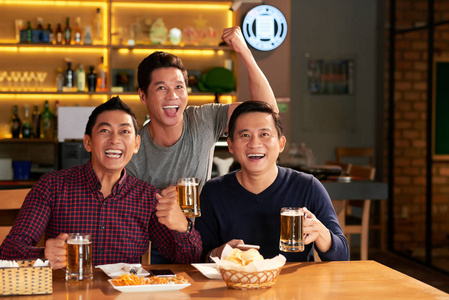 成熟的越南男子喝啤酒，支持喜爱的球队在体育酒吧