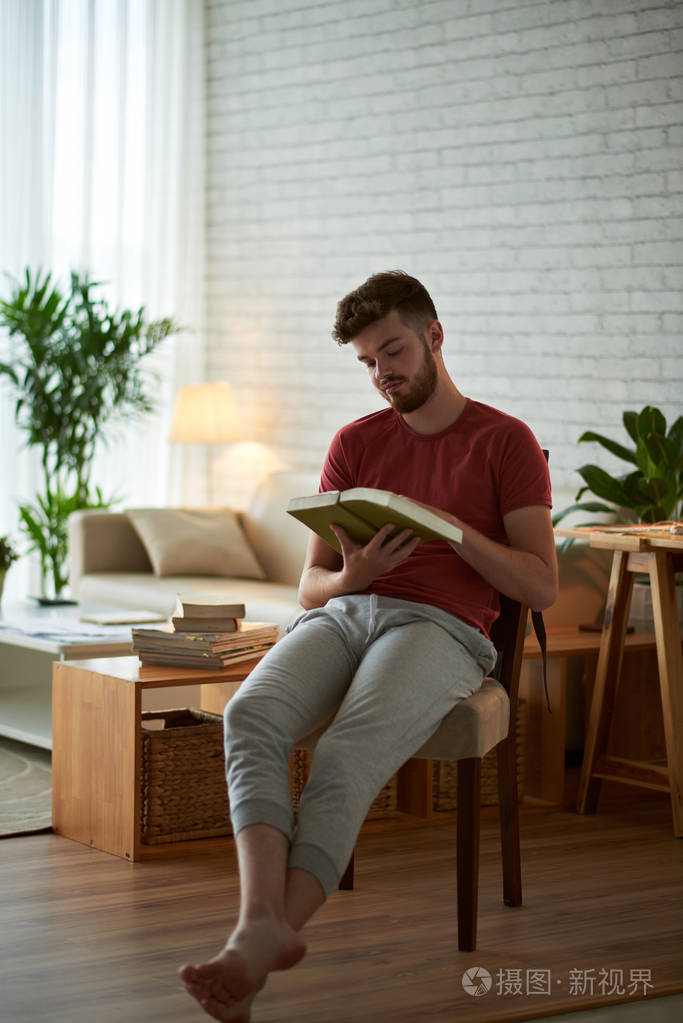 年轻人坐在家里的椅子上看书
