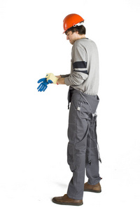 一个年轻的男子在工作灰色的衣服和橙色安全帽戴上手套的白色隔离背景