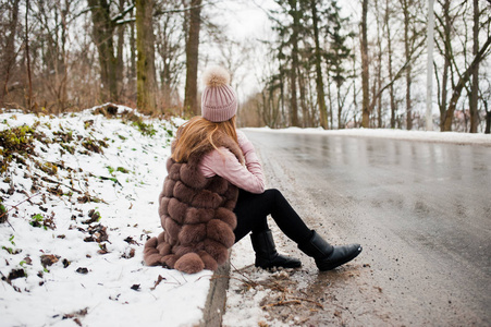 时尚的女孩在毛皮大衣和帽子在冬天的一天坐在 b