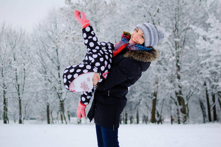 一天, 年轻漂亮的母亲和她的小女儿在雪地公园外面玩耍。活跃的妈妈抱着滑稽的女孩的手, 微笑着露的微笑
