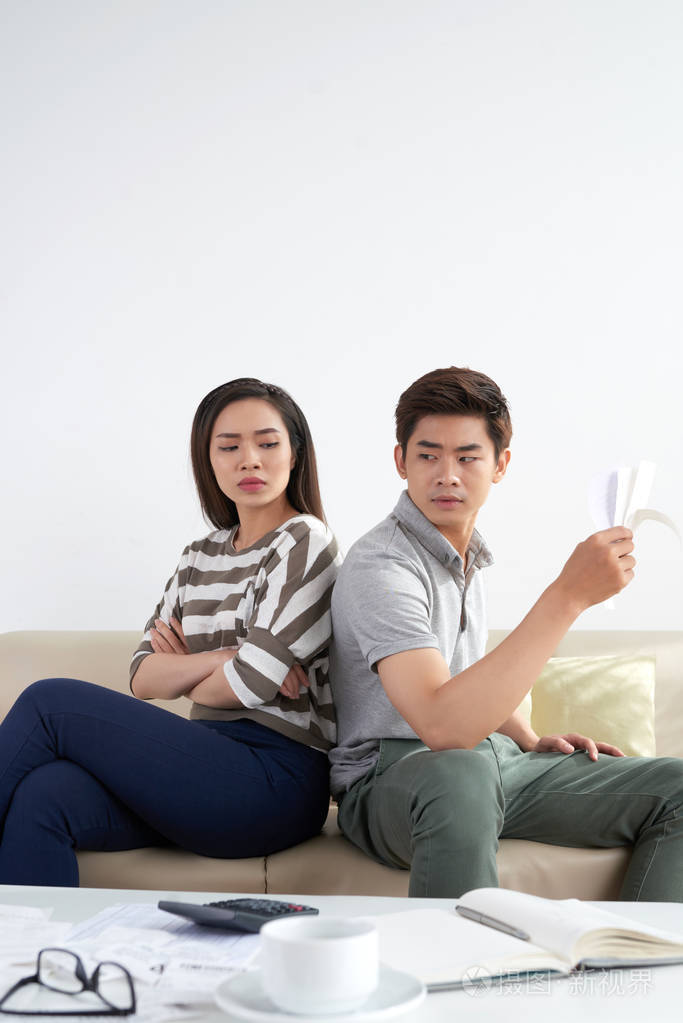 计算完家庭开支后愤恨的亚洲夫妇背靠背坐着