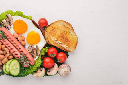 英式早餐，西红柿，香肠，豆类，蘑菇，鸡蛋和草药，俯视。 在白色的木制背景上。